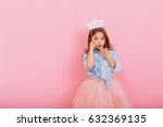 Surprised pretty young girl in tulle skirt with crown on head expressing isolated on pink background. Amazing cute little princess at carnival. Place for text