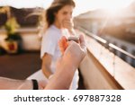 Man holding wedding ring in front of astonished happy girl covering mouth with hand. Romantic photo of charming woman standing on roof early in evening on date with boyfriend in anniversary.