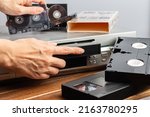 Small photo of female hand inserts VHS videocassette put into video recorder to watch video. female hand holds Old magnetic audio tape cassette for music. Retro vintage technology concept