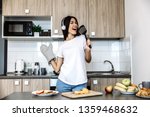 Cooking  and fun. At home. Asian girl listen music in headphones and singing in the kitchen