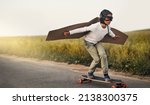 Small photo of Ready, steady, fly. Shot of a young boy pretending to fly with a pair of cardboard wings while riding a skateboard outside.