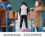 Small photo of Struggling at school. Rear view shot of an elementary school boy leaning with his head on the chalkboard in class.