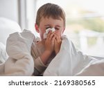 My nose wont stop dripping. Shot of a little boy feeling ill in bed at home and blowing his nose.