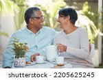 Mature couple laughing, drinking tea and bonding in backyard together, relax and cheerful outdoors. Senior man and woman enjoying retirement and their relationship,sharing a joke and tea time snack