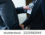 Small photo of The rotten egg in the corporate world - deceptive deals. Two corporate businessmen shaking hands while one man places money in the otherampamp pocket.