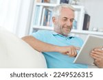 Small photo of Mature man, digital tablet or relax on sofa in house, home or apartment living room on social media app or internet game. Smile, happy or retirement person on technology crossword puzzle or streaming