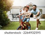 Small photo of Learning, bicycle and proud dad teaching his young son to ride while wearing a helmet for safety in their family home garden. Active father helping and supporting his child while cycling outside