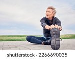 Woman, stretching exercise and fitness on blue sky mockup, park ground and training for cardio wellness. Senior female warm up legs outdoor for workout, sports running and thinking of healthy body