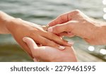 Small photo of Hands, proposal and engagement ring at lake outdoors for couple, marriage and wedding. Commitment, love and jewelry of woman and man proposing and putting band on finger for trust, care and romance.