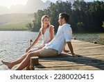 Love, laugh and pier with couple at lake for bonding, romance and affectionate date. Nature, travel and holiday with man and woman sitting on boardwalk in countryside for happy, summer and vacation
