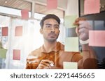 Small photo of Planning, writing and focused man on glass for project management, workflow and business schedule. Asian person brainstorming ideas, moodboard and sticky notes for solution, reminder or job priority