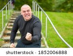 Small photo of Angry man threatening the camera with his fist as he screams abuse with a vehement expression on outdoors steps in a park