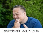 Small photo of Mischievous happy young man pointing a finger at the camera with an impish grin outdoors in a garden