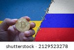 Small photo of Hand holding a bitcoin gold coin symbol of cryptocurrency on the flag of Russia and Ukraine steps with barbed wire concept illustration of tense two countries diplomatic relations between Russia and U