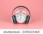 Front view of pink vintage alarm clock with headphones around on pink background with copy space.