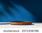 Cylinder shape wooden podium, stand and deep shadow on blue wall background. Background for product. Front view. Mockup.