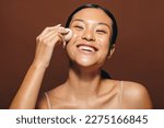 Small photo of Woman with radiant skin smiling as she applies face oil with a beauty sponge. Happy young woman gently massaging and blending a moisturising product into her skin in the midst of her skincare routine.