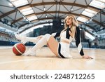 A cheerleader sits confidently on the floor, striking a pose with her foot resting on the basketball. She is dressed in a playful mini-skirt paired with knee-high socks accentuating her toned legs.