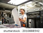 Small photo of Print shop worker checking quality of imprint and controlling printing process.