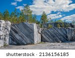Small photo of Large grey stones in an old abandoned quarry. Marble texture. Smooth cuts on the rocks. The marble quarry is horizontal. The natural stone. Marble quarry, marble rocks in the wild.