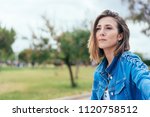 Thoughtful introvert young woman sitting outdoors in a park looking into the distance with a contemplative serious expression with copy space