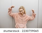 Young blonde successful girl stands in front of a metal wall and makes a victory pose with her arms