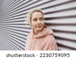 Young blonde girl stands in front of metal wall and looks to the side serious