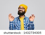 Bearded hipster in yellow hat and glasses smiling and showing dont worry be happy gesture against gray background