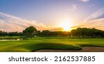 Small photo of Golf course at sunset with beautiful sky and sand trap. Scenic panoramic view of golf fairway with bunker. Golf field with pines