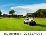 Small photo of Golf cart in fairway of golf course with green grass field with cloudy sky and trees at sunset