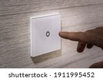 A close-up finger turns on the light on the touch switch. A white modern light switch on a white wall. modern design. turn-on turn-off