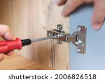 Concept of home repairing. A hand of a furniture assembler adjusting a mechanism for opening the door of the office table with a screwdriver. Close up. Self-assembly of furniture.
