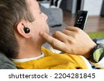 Small photo of Close-up of wireless earphone in human ear on dark background. insert the earphone into the ear. listening to music with headphones.