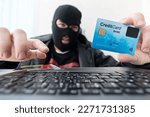 Small photo of Man in robber mask uses internet, bank account and credit facilities. Phishing attack by male with hidden face. Hacker enters stolen financial data. Confidential information was taken by fraudster.