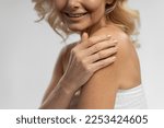 Selective focus on the hand on shoulder of a charming blonde mature woman in white towel, smiling a toothy smile, isolated on white background. Cosmetology Dermatology Aesthetic medicine concept