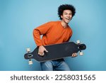 Happy attractive African American man holding longboard simulate playing guitar, having fun isolated on blue background. Portrait of attractive  overjoyed skater looking at camera. Positive emotions