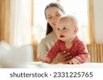 Small photo of Cute nanny takes care of adorable child in kindergarten, holding her, smiling. Selective focus on baby. Toddler care concept