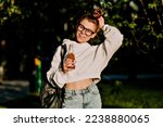 Small photo of Adorable lovely cite girl in white shirt and jeans in glasses is holding fresh juice and going to study in sunny morning .