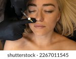 Doctor adds volume to woman's lips with lip filler, injection. White female lying on couch. Beauty physician holds syringe near girl's face.Lip augmentation procedure.Cosmetologist,aesthetic medicine