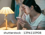 Small photo of Tired Asian woman stay up late browsing website online overused eyes hurting painful. sick exhausted female massage nose bridge to release pain. frowning girl using smart phone by lamp in dark night.