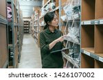 Small photo of beautiful young asian woman worker of clothes factory doing stock taking in warehouse. girl employee counting products in stockroom. elegant lady staff in storehouse holding clipboard and pen working