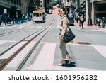 full length side view of young pretty stylish asian chinese female crossing zebra road of san francisco usa. historic cable cars riding on famous california street at dawn on sunny day in busy urban