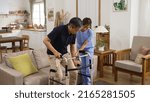 Small photo of asian Japanese older male stroke patient practicing using a walker with the assistance of his personal care attendant in the living room at home