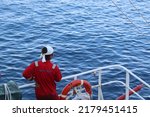 Small photo of a sailor with a coverall and a headband is standing near the ship's railing and looking at the wide sea as if releasing heavy work. healing