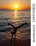 Small photo of Silhouette of young gymnast woman doing handspring on sandy beach at sunset. Happy child doing cartwheel on the sunny beach sand