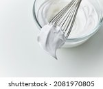 Small photo of glass bowl of whipped egg whites cream on white kitchen table background, top view