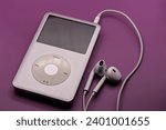 Small photo of Brooklyn, NY - Dec 14 2023: Apple Ipod classic mp3 player with white headphones on a solid pink background.