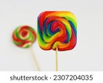 Small photo of Multicolored square lollipop, sweet candy in rainbow colors after expiry date. Lollypop on white background with another colorful lollipops blurred behind, ugly food