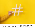 Social media concept, closeup of human hand holding and showing large big white hashtag sign