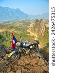 Small photo of NAM XAY VIEWPOINT, VANG VIENG, LAOS - FEBRUARY 16, 2024: Ancient motorcycle parked and Lao flag on the Nam Xay Viewpoint, During the dry season in Laos.